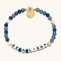 Bracelet with blue and white beads and a gold tag on a white background