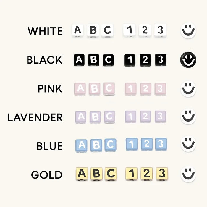 Letter bead color swatch guide showing white, black, pink, lavender, blue, and gold cube bead options with matching smiley face beads on a white background