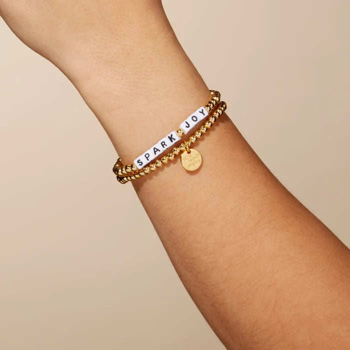Gold bracelet with  text on a wrist against a beige background