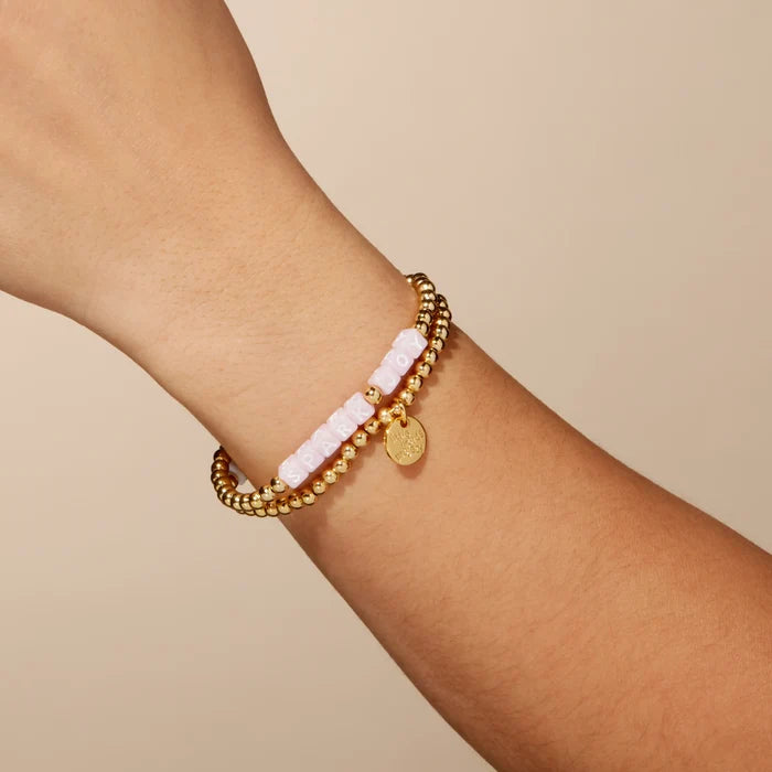 Gold bracelet with pink beads on a wrist against a beige background