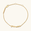 A delicate gold chain bracelet with a personalized script nameplate reading 'your text' and a lobster clasp, shown on a light cream background.