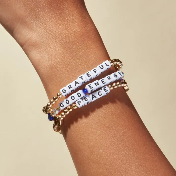 Bracelets with motivational phrases on a wrist against a beige background