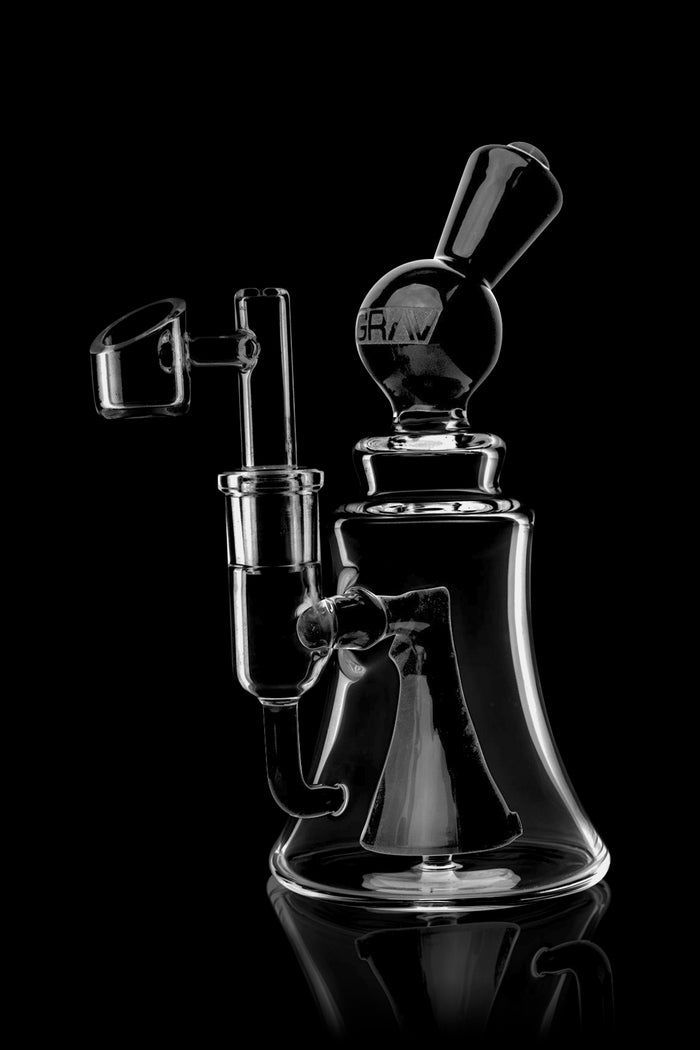 Clear glass dab rig with intricate design, reflecting on a black surface.