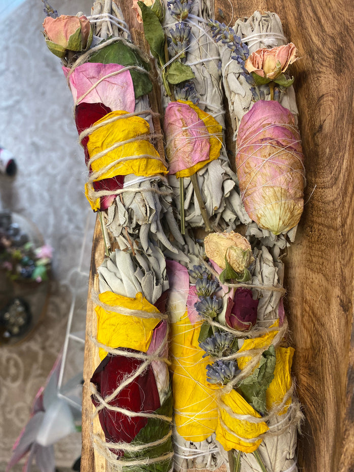 Several white sage smudge sticks wrapped with pink rosebuds and yellow and red flower petals