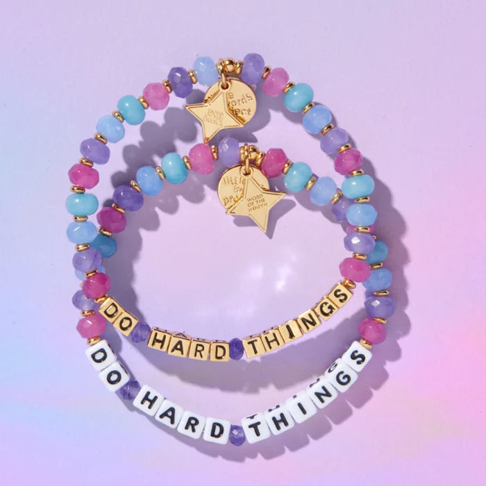 Do Hard Things September Word of the Month bracelets in both white letter beads and gold letter beads laid flat on a pastel purple background