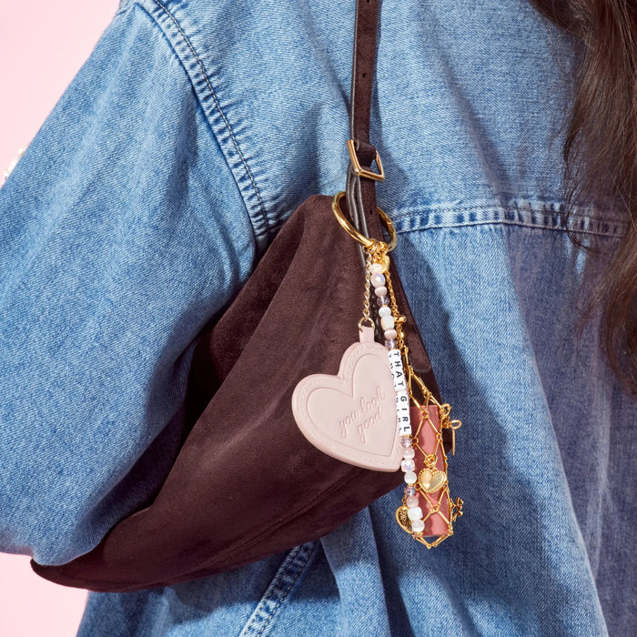 Brown bag with heart-shaped keychain and decorative elements worn by a person in a denim jacket.